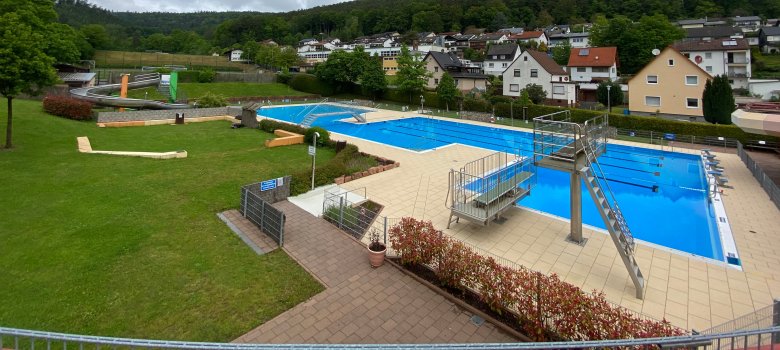 Blick auf das Becken mit Sprungturm und Einmeter-Brett, Kinderbecken und Liegewiese